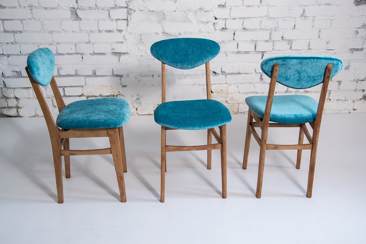 Trzy krzesła z niebieską tapicerką na tle białej sciany